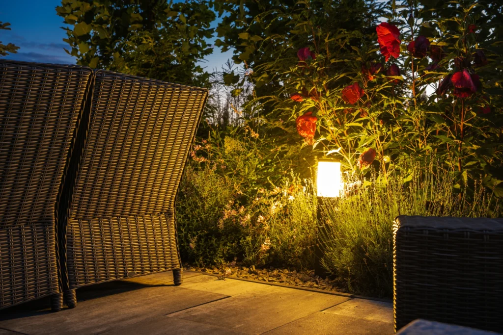 Low voltage bollard path light glowing in a garden bed beside a patio at dusk